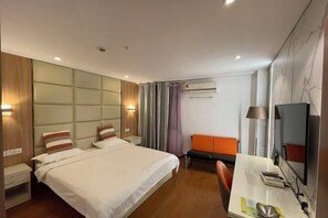 A hotel room with a bed, bedside tables, a desk, a chair, a TV, and a window with curtains.