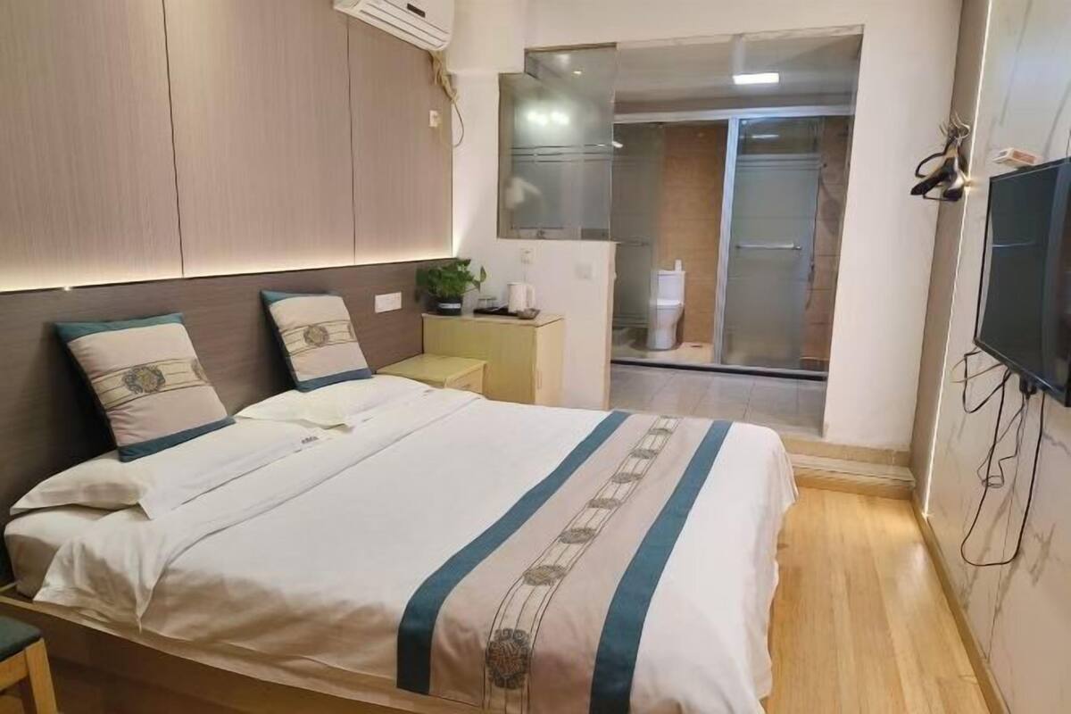 Een slaapkamer met een bed, nachtkastje, televisie en een schuifdeur naar een badkamer.