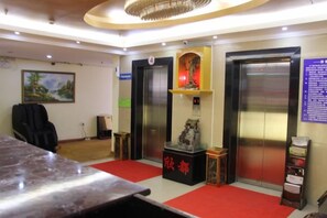 A hotel lobby with a reception desk, two elevators, a red carpet, and a wall-mounted information board. - Shanghai Xindu Business Hotel (Shanghai)