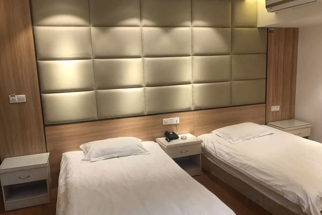 Habitación de hotel con dos camas, cabecero acolchado, mesitas de noche y un pequeño mueble auxiliar.