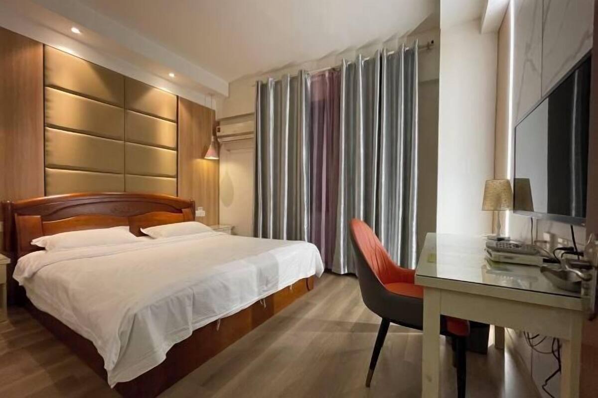 Een hotelkamer met een houten bed, een bureau met stoel, een televisie en een raam met gordijnen.