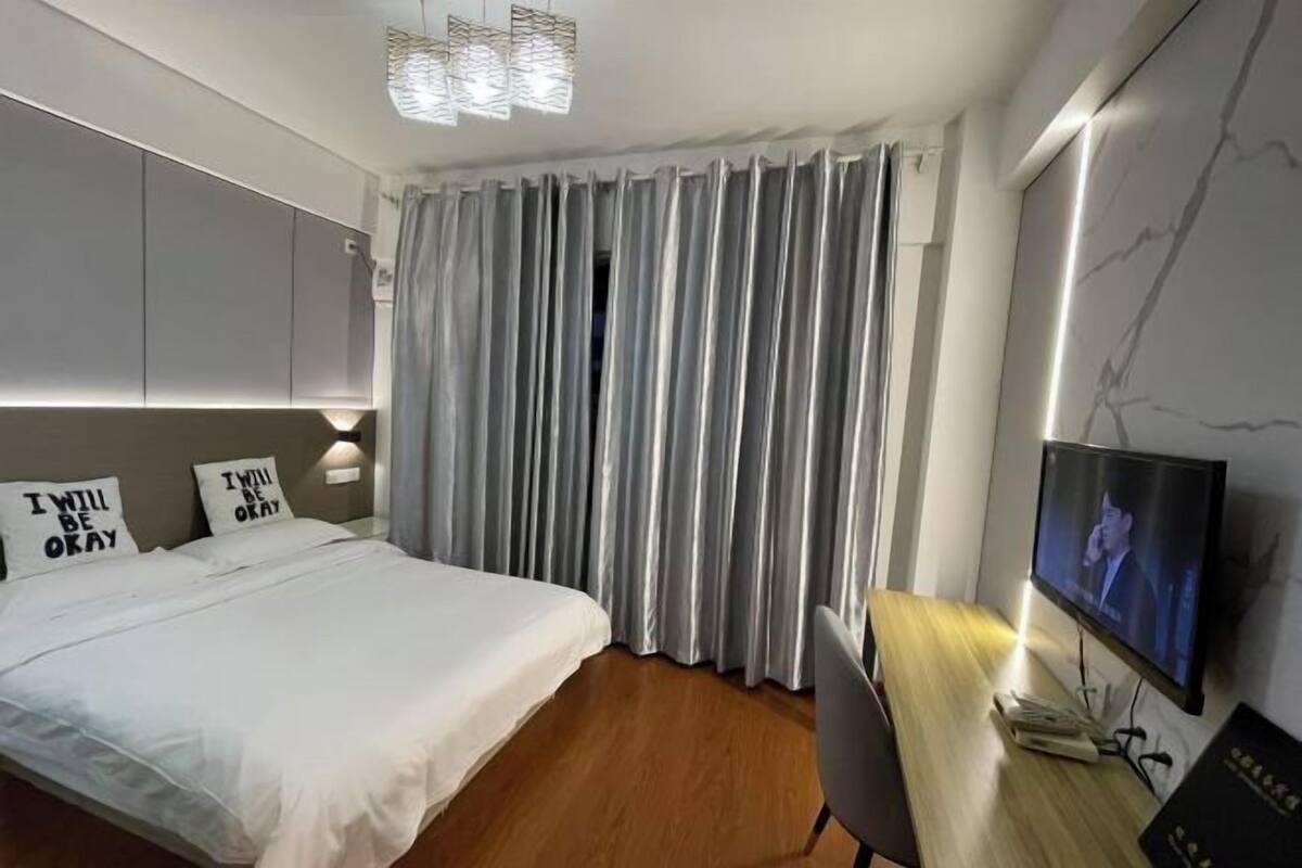 Een moderne hotelkamer met een bed, een bureau met een televisie en een groot raam met gordijnen.