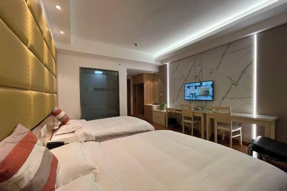 Een hotelkamer met twee bedden, een bureau met stoel, een televisie en een wand met marmerprint.