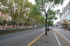 A tree-lined street with buildings on one side and a sidewalk on the other. - Shanghai Xindu Business Hotel (Shanghai)