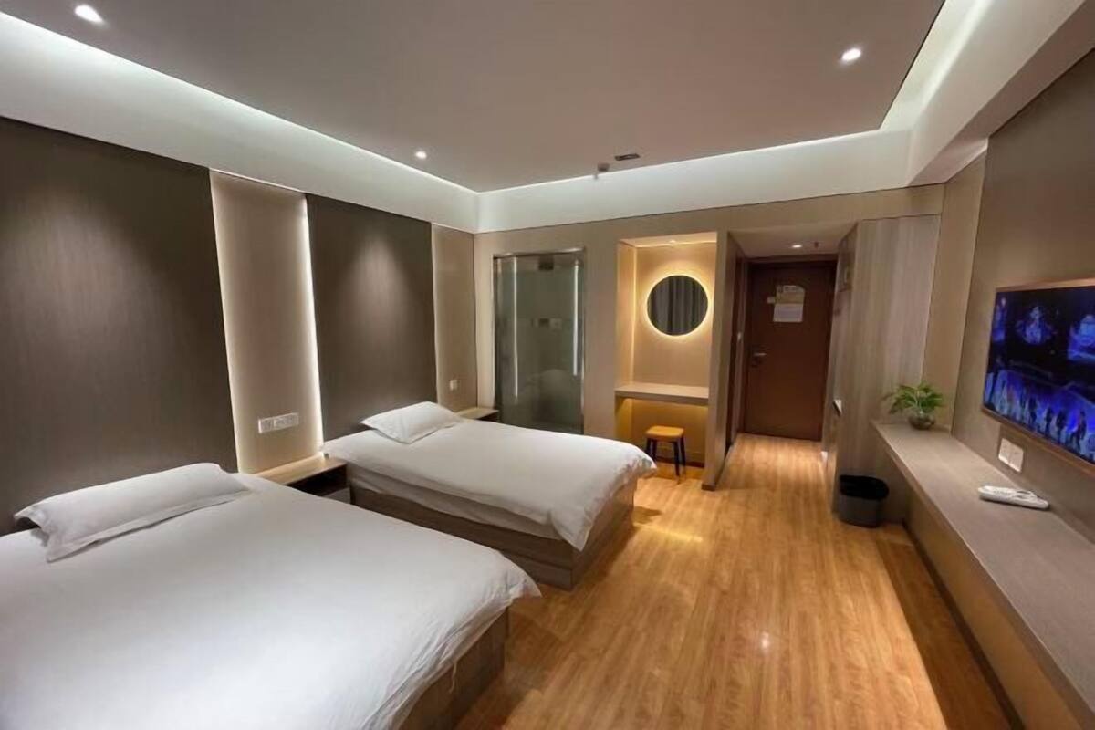 Een hotelkamer met twee bedden, een televisie, een klein krukje en een spiegel.