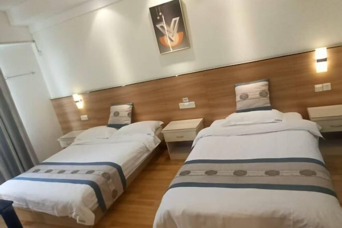 Een hotelkamer met twee bedden, een houten hoofdbord, nachtkastjes en wandlampen.