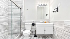 Une salle de bain moderne avec une douche à parois de verre, des toilettes blanches, un meuble-lavabo avec un miroir et un sol à motifs de marbre.