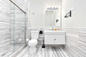 A modern bathroom with a glass shower enclosure, a white toilet, a vanity with a mirror, and a marble-patterned floor.