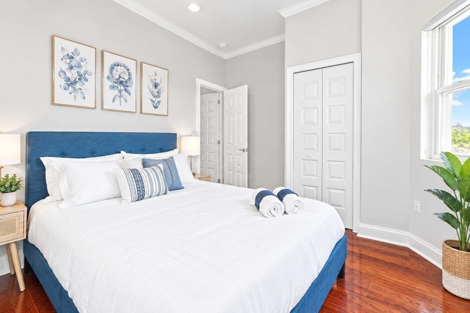 A bedroom with a large bed, a nightstand, a lamp, and a potted plant.
