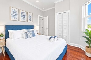A bedroom with a large bed, a nightstand, a lamp, and a potted plant.