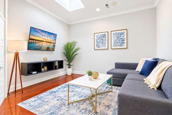 A modern living room with a sofa, a coffee table, a floor lamp, a painting, and two framed artworks.