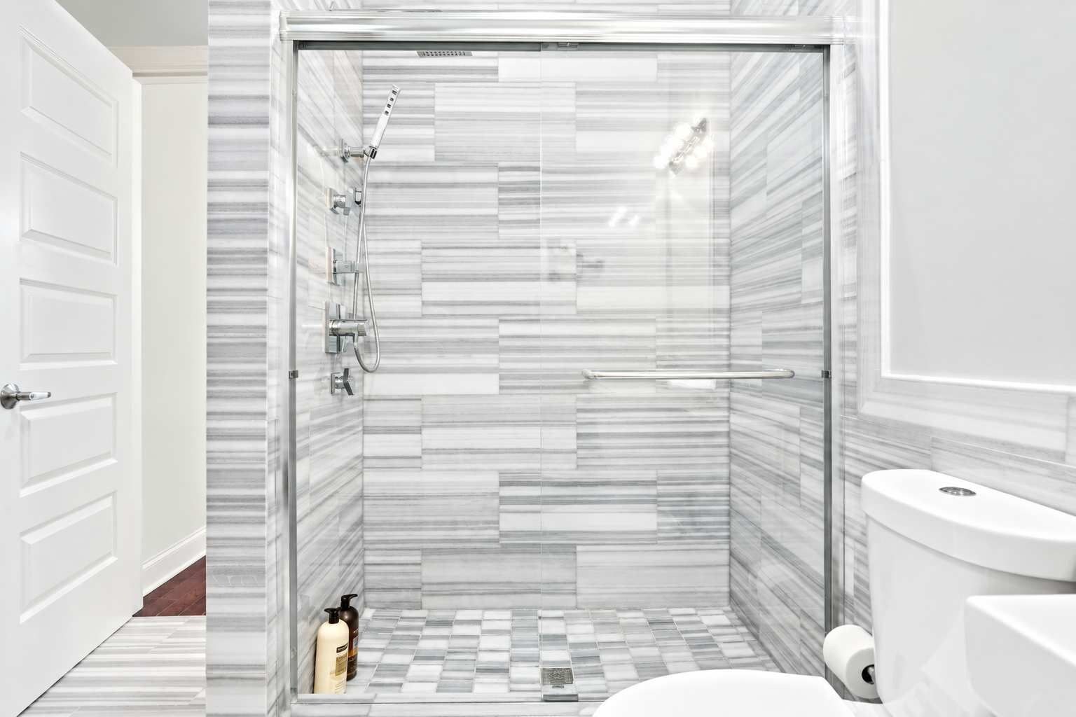 A modern bathroom with a shower, toilet, and a tiled floor.