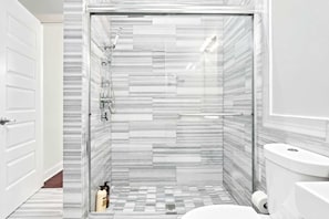 Um banheiro moderno com chuveiro, vaso sanitário e piso em azulejo.