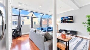Una sala moderna con un sofá gris, sillones azules, una mesa de centro de madera y un televisor de pantalla plana montado en la pared.