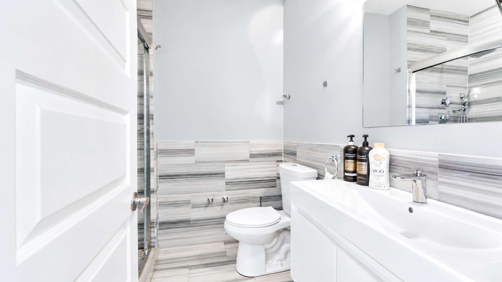 Un baño moderno con inodoro y lavamanos blancos, y un espejo sobre el lavamanos.