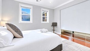 Une chambre à coucher avec un lit, deux fenêtres, une chaise et un tableau blanc.