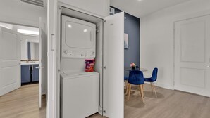 A modern kitchen with a built-in washer and dryer, a dining area with a table and chairs, and a hallway leading to another room. - Luxury Modern 2BR Sleeps 8 | near Fair Park Dallas (Dallas)