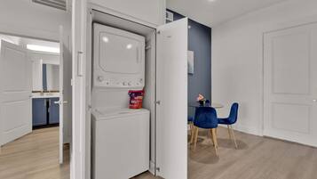 Una cocina moderna con lavadora y secadora integradas, un comedor con mesa y sillas, y un pasillo que conduce a otra habitación.