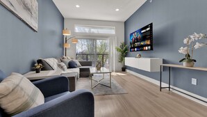 A modern living room with a sofa, armchairs, a coffee table, a TV mounted on the wall, and a potted plant. - Luxury Modern 2BR Sleeps 8 | near Fair Park Dallas (Dallas)