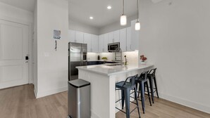 A modern kitchen with white cabinets, stainless steel appliances, a central island with bar stools, and pendant lighting. - Luxury Modern 2BR Sleeps 8 | near Fair Park Dallas (Dallas)
