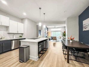 A modern kitchen with a central island, stainless steel appliances, and a dining area with a dark wood table and chairs. - Luxury 3BD | Deep Ellum | Parking | Pool+Gym (Dallas)