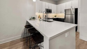 Une cuisine moderne dotée d’un îlot central, d’appareils électroménagers en acier inoxydable et de luminaires suspendus.
