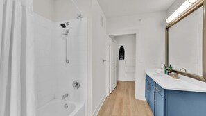 A modern bathroom with a bathtub, shower, and a vanity with a mirror. - Upscale 2BD Deep Ellum | Parking | Pool | Gym Pass (Dallas)