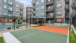 A tennis court with a net, surrounded by a fence, and adjacent to a swimming pool. - Upscale 2BD Deep Ellum | Parking | Pool | Gym Pass (Dallas)
