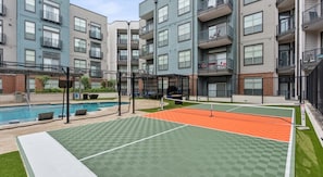 A tennis court with a net, surrounded by a pool and a building with balconies. - Upscale 2BD Deep Ellum | Parking | Pool | Gym Pass (Dallas)
