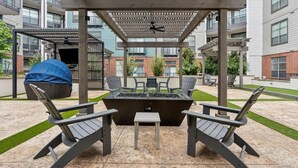 An outdoor patio area with a fire pit, two Adirondack chairs, and a covered seating area. - Upscale 2BD Deep Ellum | Parking | Pool | Gym Pass (Dallas)