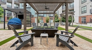 An outdoor patio area with a fire pit, two Adirondack chairs, and a covered seating area. - Upscale 2BD Deep Ellum | Parking | Pool | Gym Pass (Dallas)