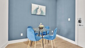 A dining area with a round glass table, four blue chairs, and a decorative bowl with lotus flowers.