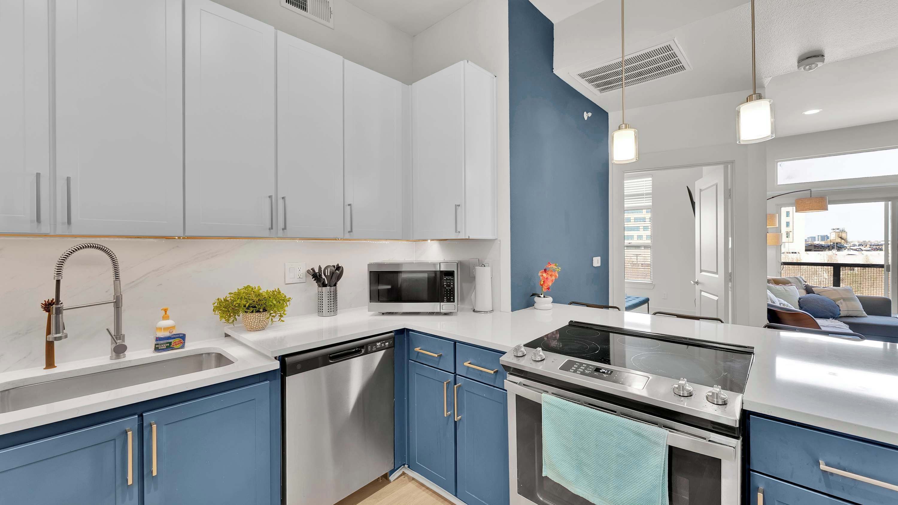 A modern kitchen with white and blue cabinetry, stainless steel appliances, and a view to the outside.