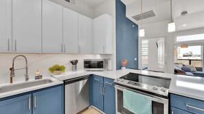 A modern kitchen with white and blue cabinetry, stainless steel appliances, and a view to the outside.