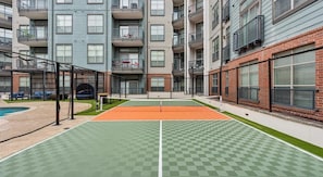 An outdoor tennis court with a net, surrounded by apartment buildings. - Upscale 2BD Deep Ellum | Parking | Pool | Gym Pass (Dallas)