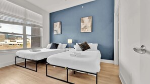 A hotel room with two beds, a view of buildings outside, and artwork on the wall. - Upscale 2BD Deep Ellum | Parking | Pool | Gym Pass (Dallas)
