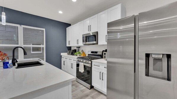 A modern kitchen with white cabinets, stainless steel appliances, a built-in oven, and a microwave.