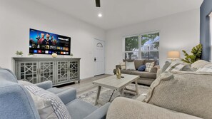A living room with a flat-screen TV, grey sofa, coffee table, and a cabinet with glass doors.
