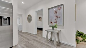 A hallway with a water dispenser, a round decorative mirror, a framed floral artwork, and a small table with a plant.