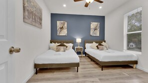 A bedroom with two beds, a nightstand, a ceiling fan, and artwork on the walls.