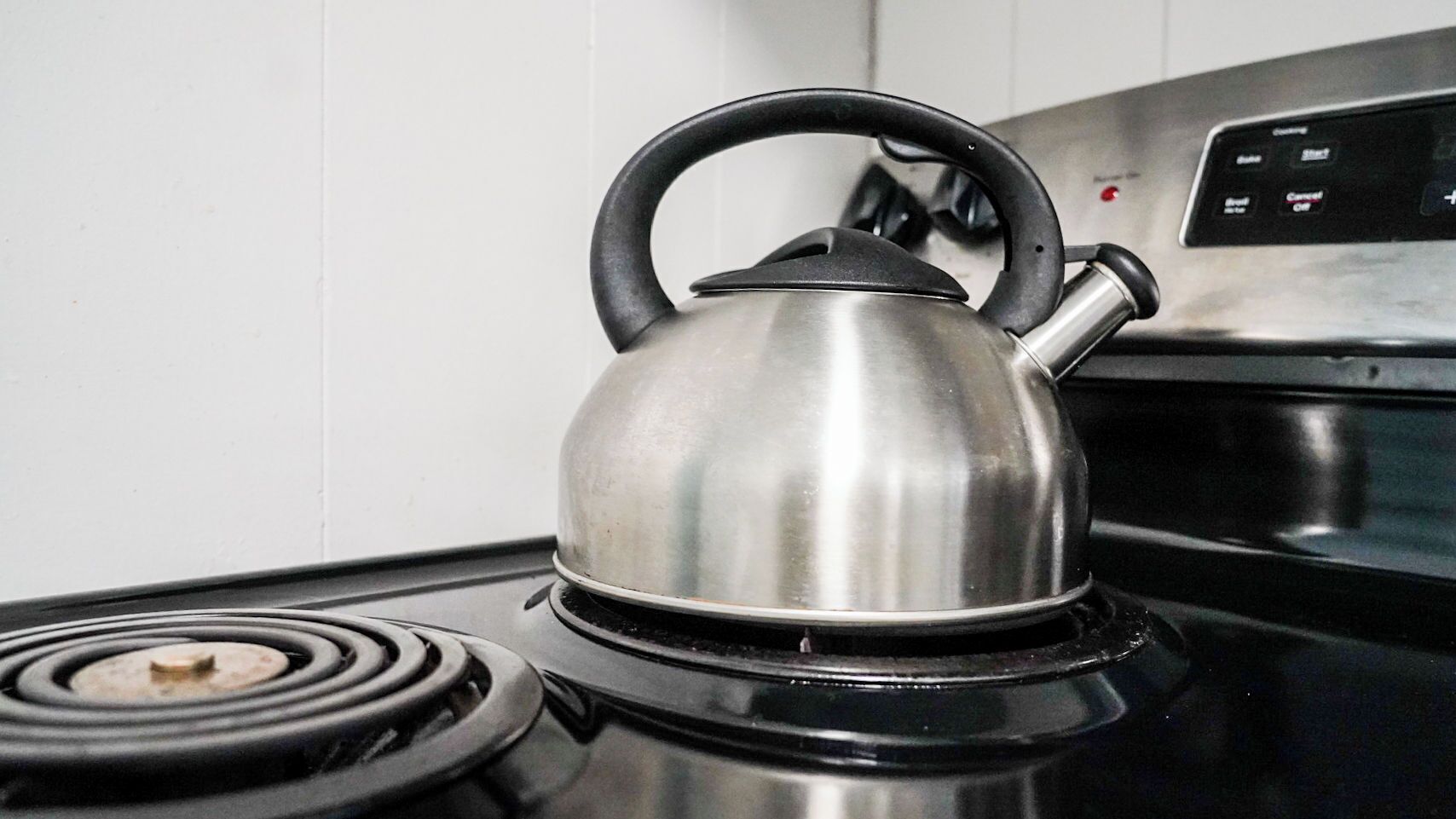 Une bouilloire en acier inoxydable posée sur une plaque de cuisson noire, avec un panneau de commande en arrière-plan.