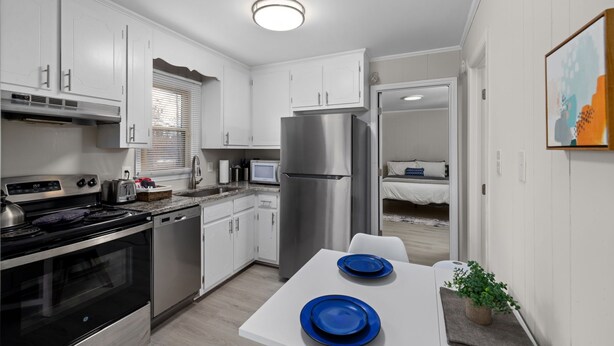 A compact kitchen with white cabinets, stainless steel appliances, and a dining area with blue plates. - Stylish & Cozy 1BR Apt Near Duke, Downtown Durham, Dining & Entertainment (Durham)