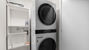 A laundry area with two stacked washing machines and a white laundry basket. - Stylish & Cozy 1BR Apt Near Duke, Downtown Durham, Dining & Entertainment (Durham)