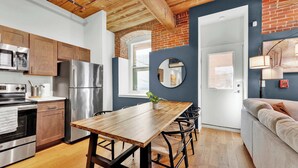 A modern kitchen with stainless steel appliances, a wooden dining table, and a brick wall. - Luxury 2BD | 4 Beds | Northern Liberties (Philadelphia)