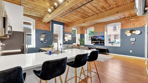 A modern kitchen with a central island, bar stools, and a dining area with a large window. - Luxury 2BD | 4 Beds | Northern Liberties (Philadelphia)