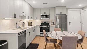 A modern kitchen with white cabinets, stainless steel appliances, and a marble dining table. - Luxury 1BD | 1 Bed | Northern Liberties (Philadelphia)