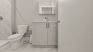 A modern bathroom with a toilet, a sink with a mirror above it, and a shower area. - Luxury 1BD | 1 Bed | Northern Liberties (Philadelphia)