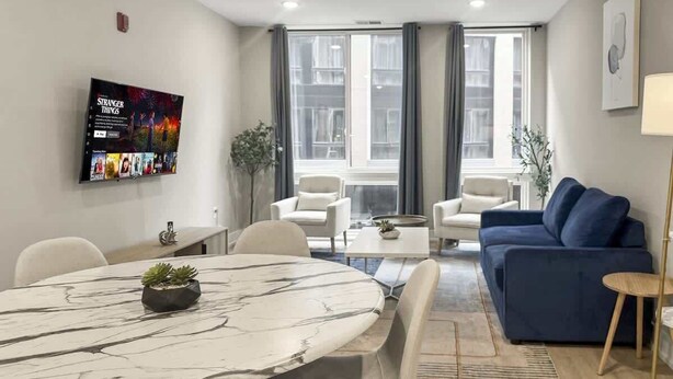 A modern living room with a marble dining table, a blue sofa, and a flat-screen TV mounted on the wall. - Luxury 1BD | 2 Beds | Northern Liberties (Philadelphia)