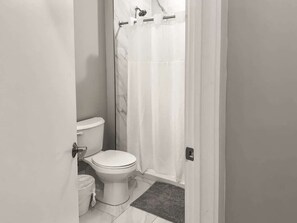 A small, compact bathroom with a toilet, a shower curtain, and a rug.
