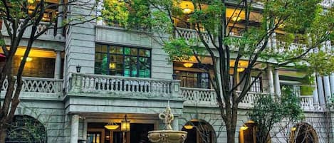 Un edificio de varios pisos con una entrada imponente, amplias ventanas y una fuente.